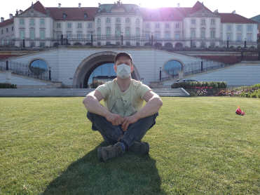 Greg guia de Varsovia em mascara com Castelo Real de Varsovia no fundo
